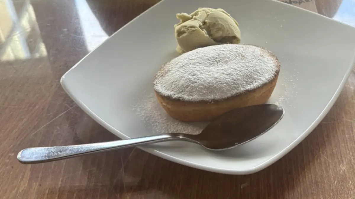 A tonda-style dessert dusted with icing sugar beside a quenelle of gelato on a white square plate